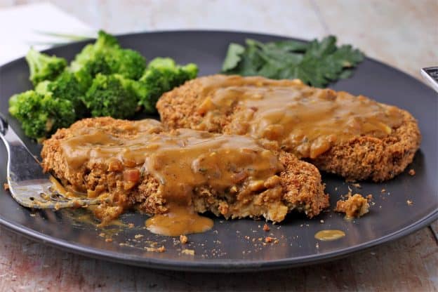 Chickpea cutlets are smothered in mustard sauce on a black plate and cut with a fork.