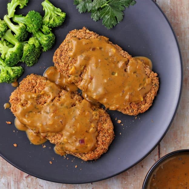 Overhead shot of 2 chickpea cutlets with mustard sauce and broccoli on a black plate.