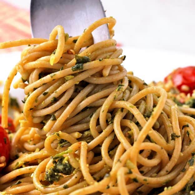 Spaghetti with pesto and cherry tomatoes is swirled with a fork.