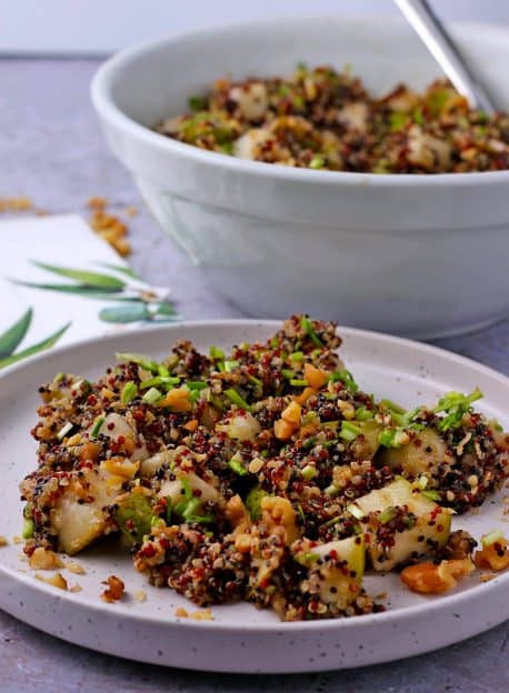 Rainbow quinoa and pear salad on white plate with chopped walnuts and chives.