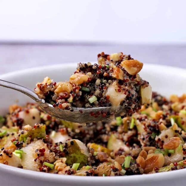 A spoonful of rainbow quinoa and pear salad is held of a bowl of salad.