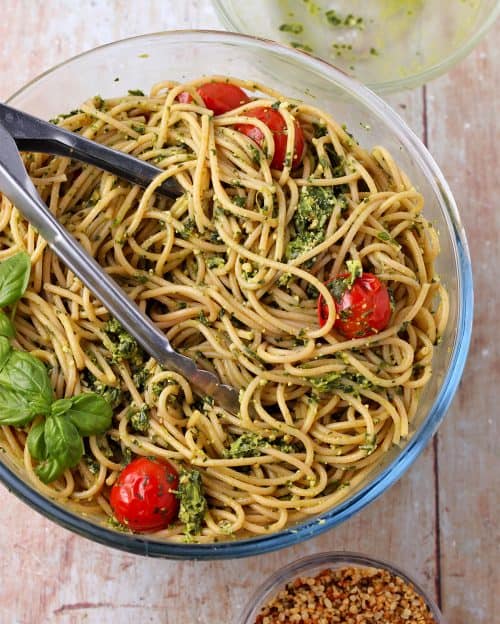 Spaghetti al pesto with blanched cherry tomatoes in glass bowl with hemp Parmesan.