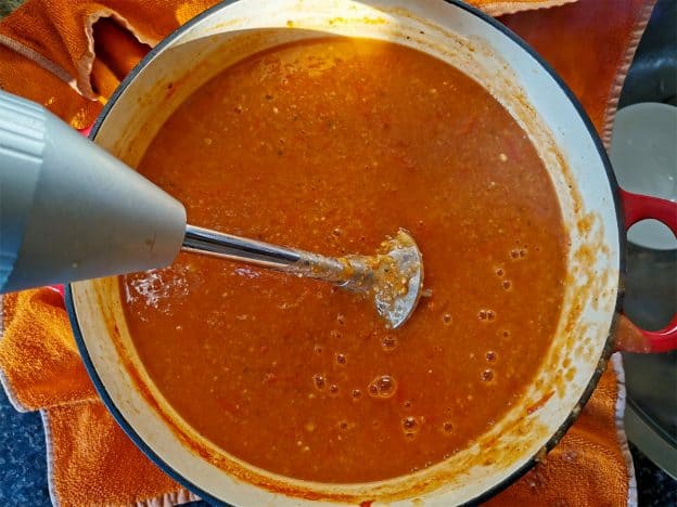Vegan tortilla soup is pureed with an immersion blender.