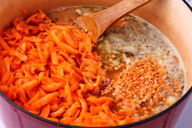 Shredded carrots, split red lentils and plant milk is added to a soup pot.