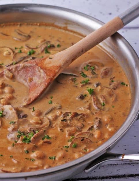 A skillet filled with chickpeas and mushrooms in sour cream sauce.