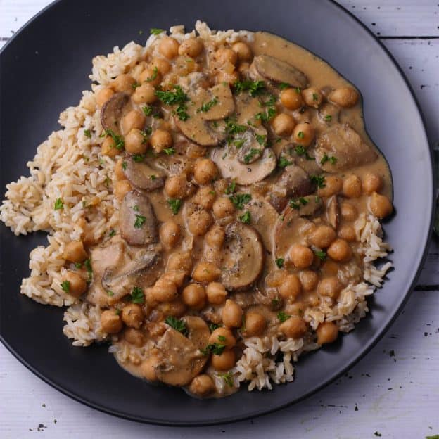 Creamed chickpeas and mushrooms over rice on a black plate.