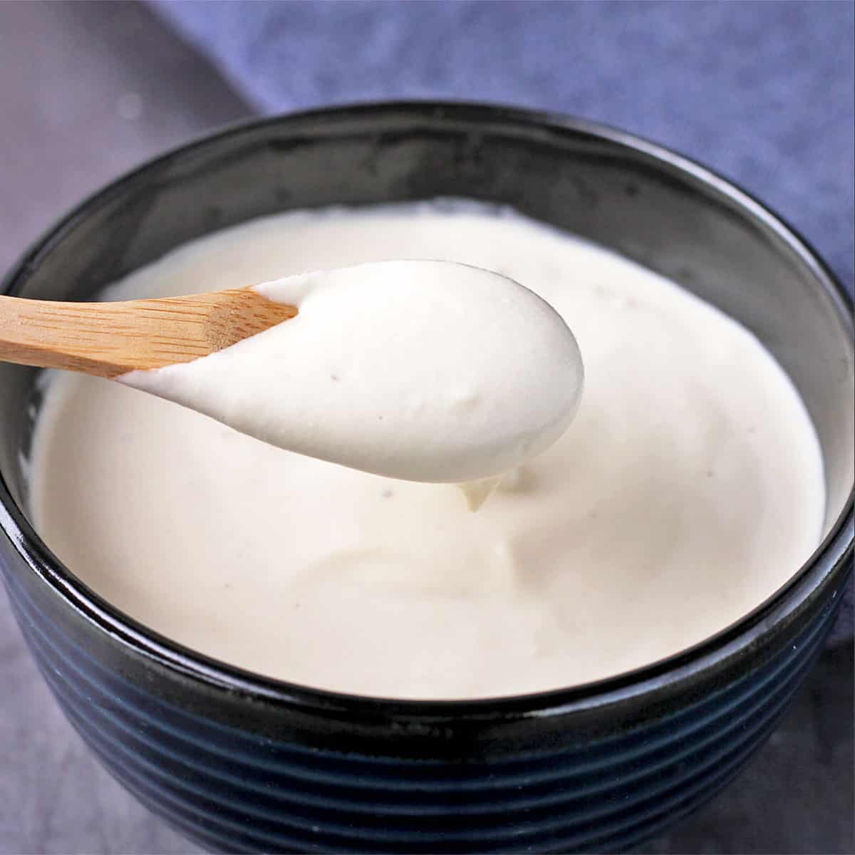A small wooden spoonful of plant-based sour cream is held over a blue bowl.