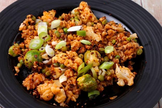 Paella rice with cauliflower, Brussels sprouts, green peas, and sliced scallions on a black plate.