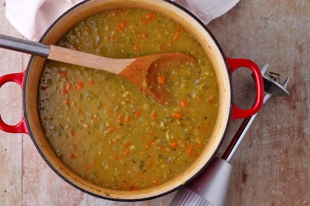 A red pot with split pea soup with carrots, celery, and onions before being blended.