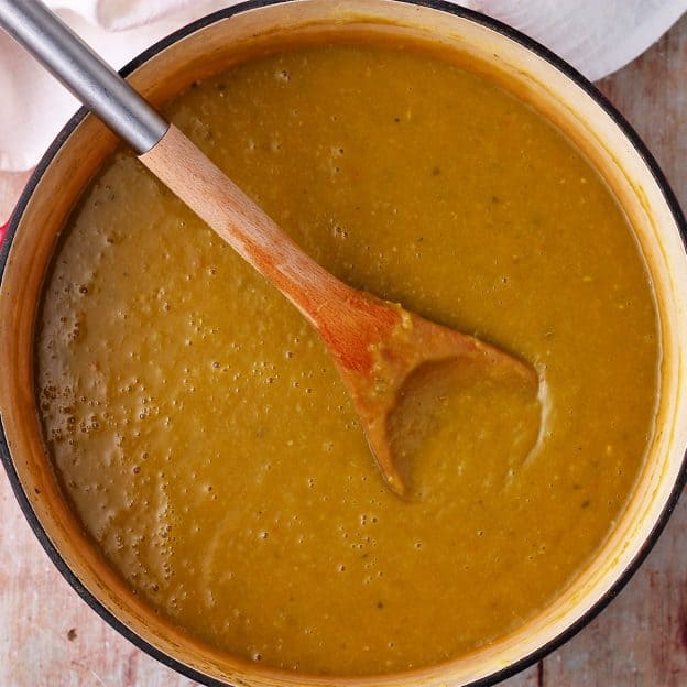 Blended vegan split pea soup in a soup pot with a wooden spoon.