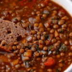 Bread is dipped into a white bowl of vegan French lentil soup.