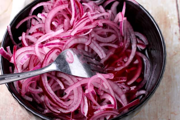 Quick pickled red onions in a black bowl with a spoon.