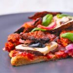 Quinoa crust pizza with tomato sauce and mushrooms and toppings on a gray plate.