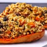 Halves of baked vegan stuffed butternut squash with dried cranberries and chopped walnuts.