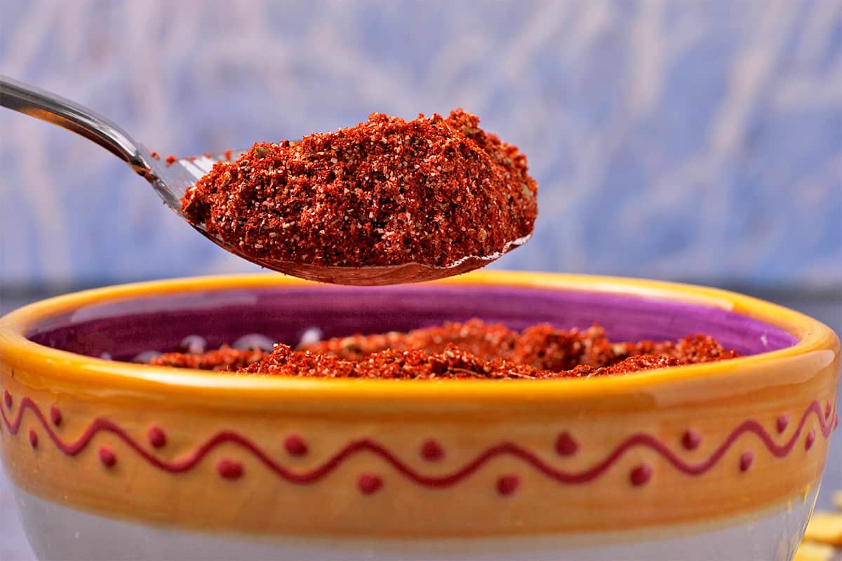 Homemade chili powder is held in a spoon over a yellow bowl.