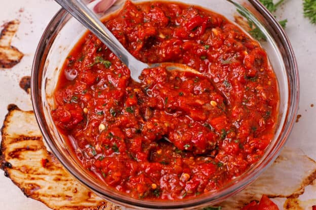 A glass bowl is filled with roasted red pepper harissa paste.