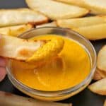 A roasted chip is dipped in vibrant curry dipping sauce.
