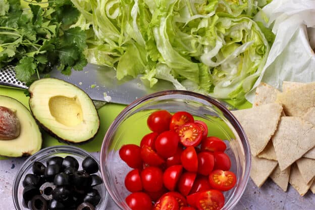 Sliced cherry tomatoes, black olives, a cut avocado, shredded lettuce, and homemade tortilla chips.