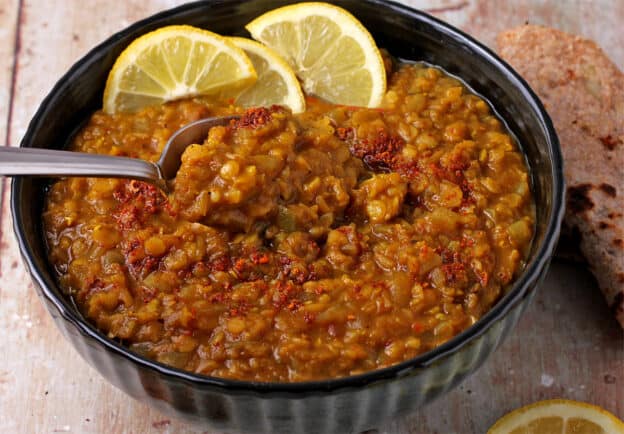A bowl with a spoon filled with cooked red lentils with tomatoes and spices.