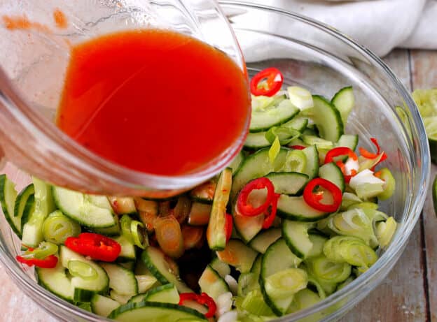 Dressing is poured over a cucumber salad.