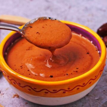 A spoonful of spicy chipotle salad dressing it held over a bowl.
