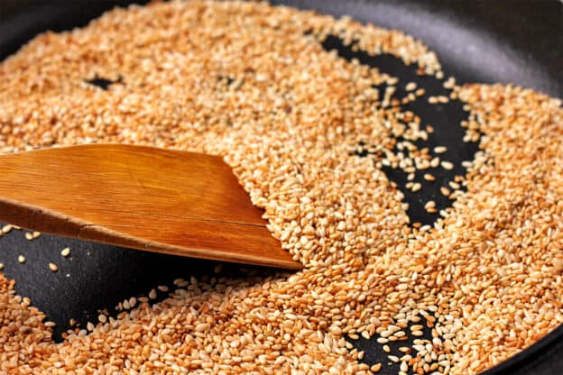 Sesame seeds are toasted in a pan and stirred with a wooden spoon.
