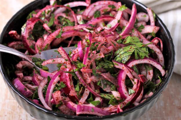 Red onions with parsley, sumac, and rice vinegar are placed in a bowl.