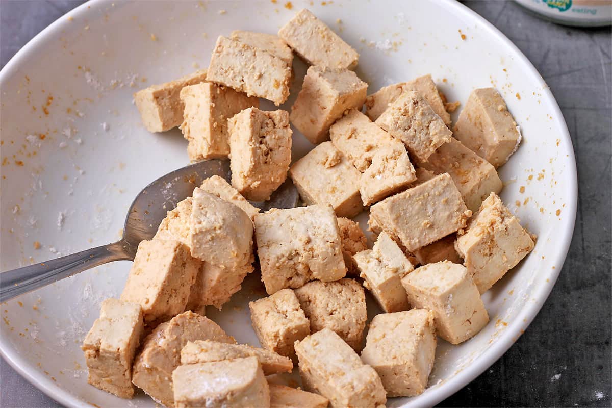 Cornstarch is tossed onto cubes of tofu in a bowl.