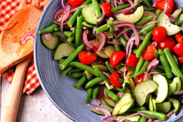 A blue bowl filled with cucumbers, green beans, red onions, and cherry tomatoes in dressing.