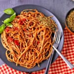 Spaghetti arrabbiata on a black plate with a fork and spoon.