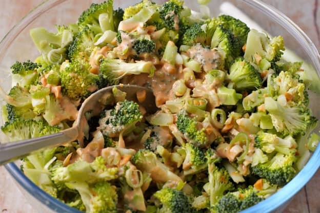 Tahini dressing is mixed into broccoli slaw with a spoon.