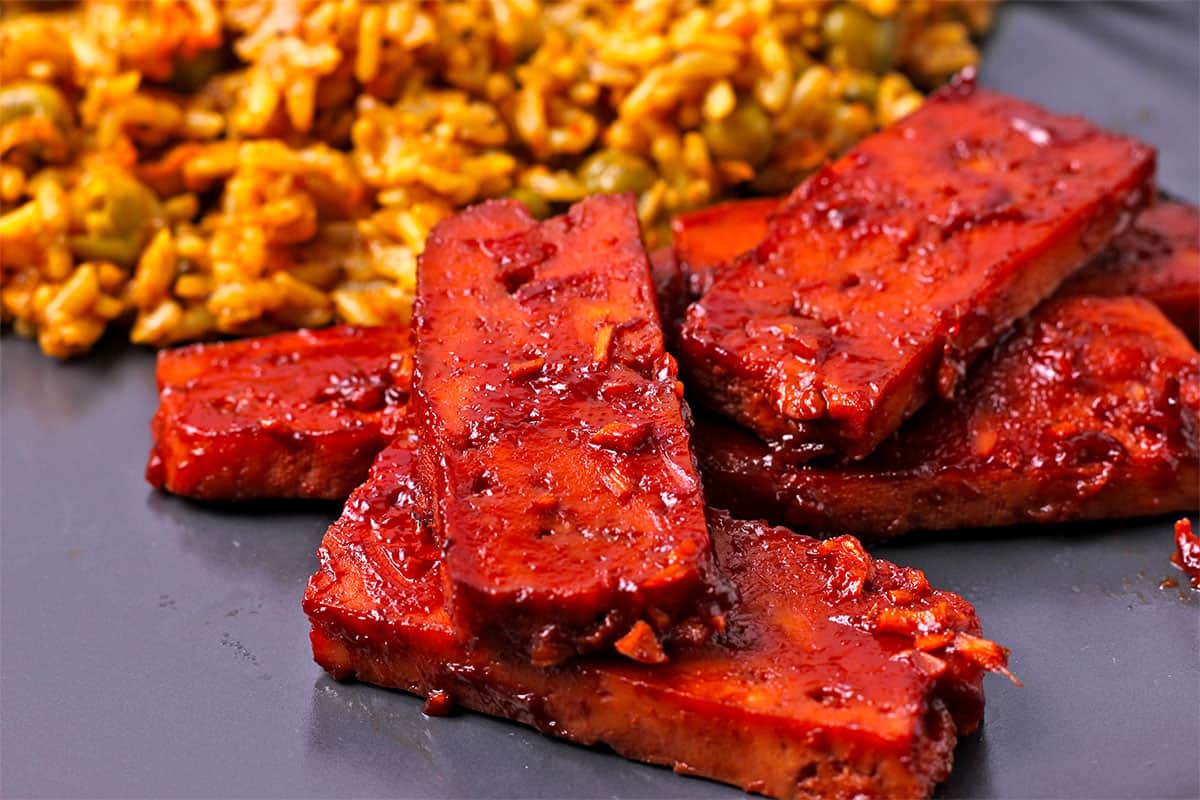Sliced of tofu with Huli Huli sauce is served on a plate with rice.