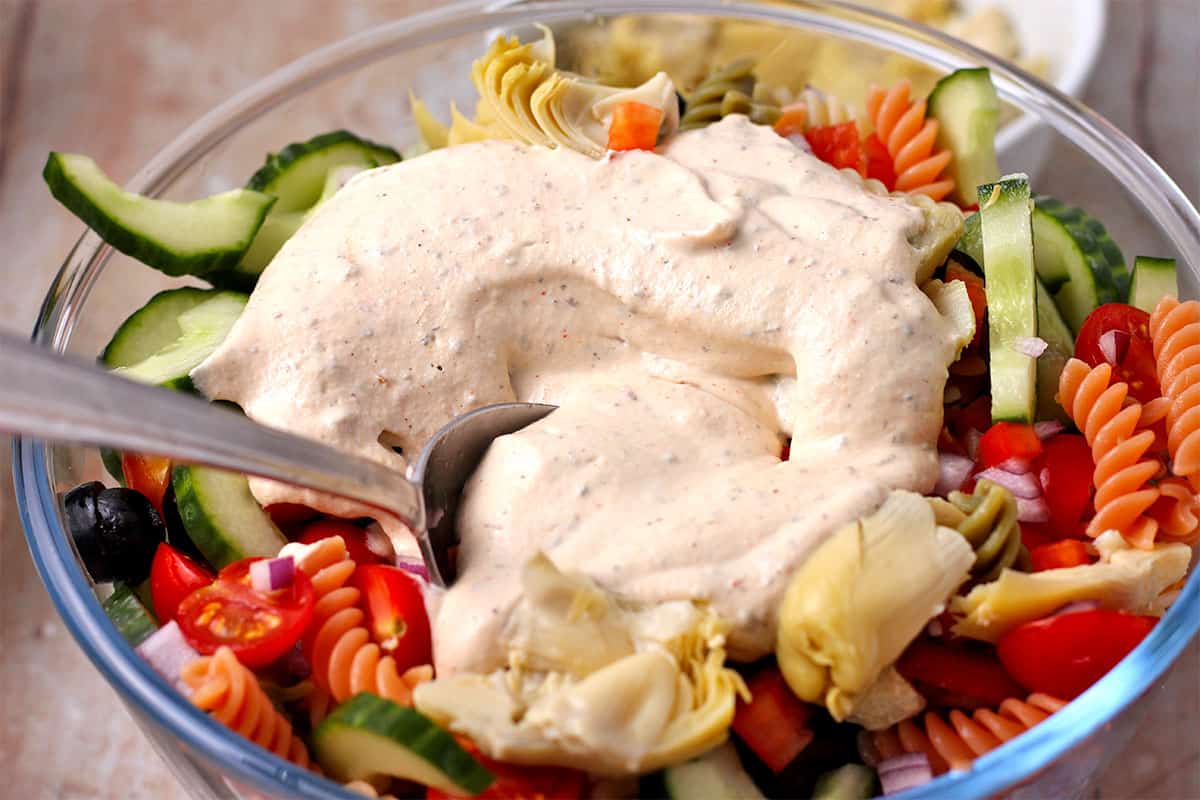 Dressing is added to pasta salad with vegetables.