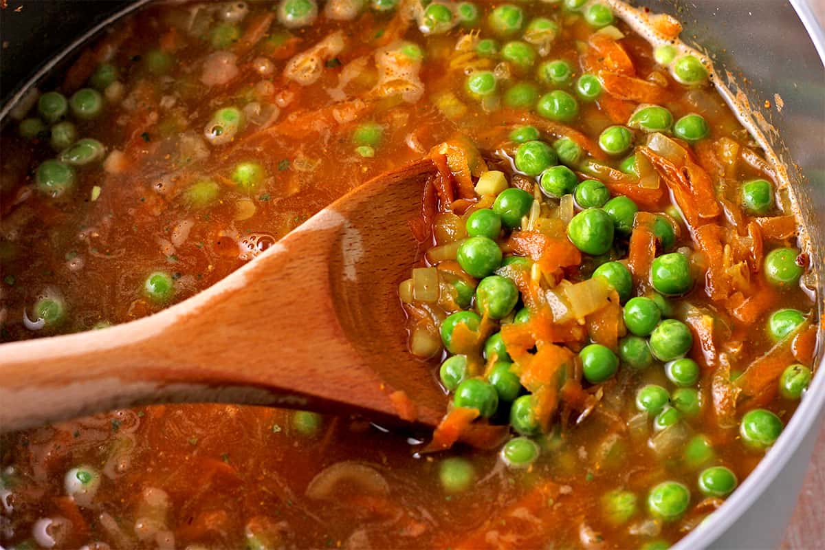 Peas are stirred into a pot of vegetables and rice.