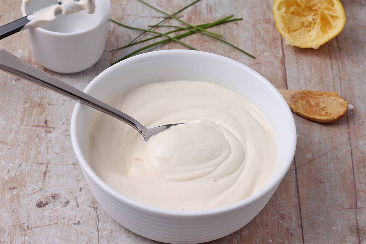 A white bowl with homemade vegan mayo and a spoon.