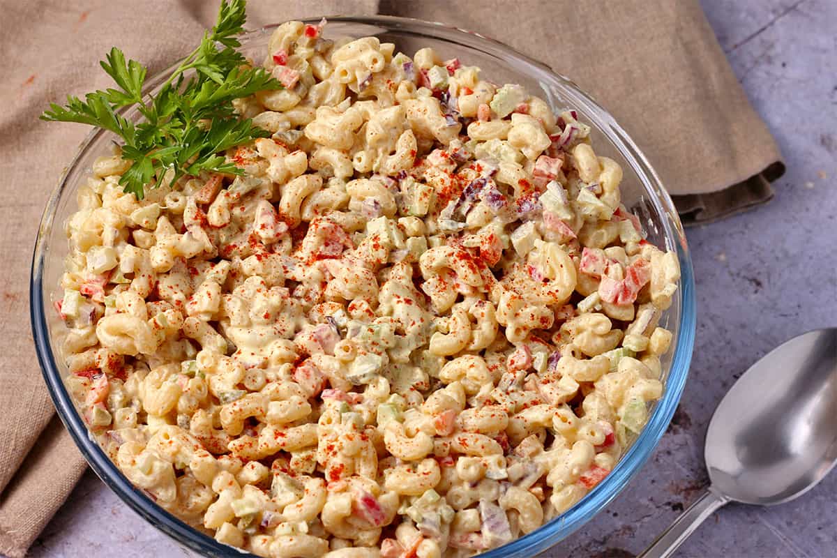 A bowl filled with creamy macaroni salad with paprika and parsley on top.