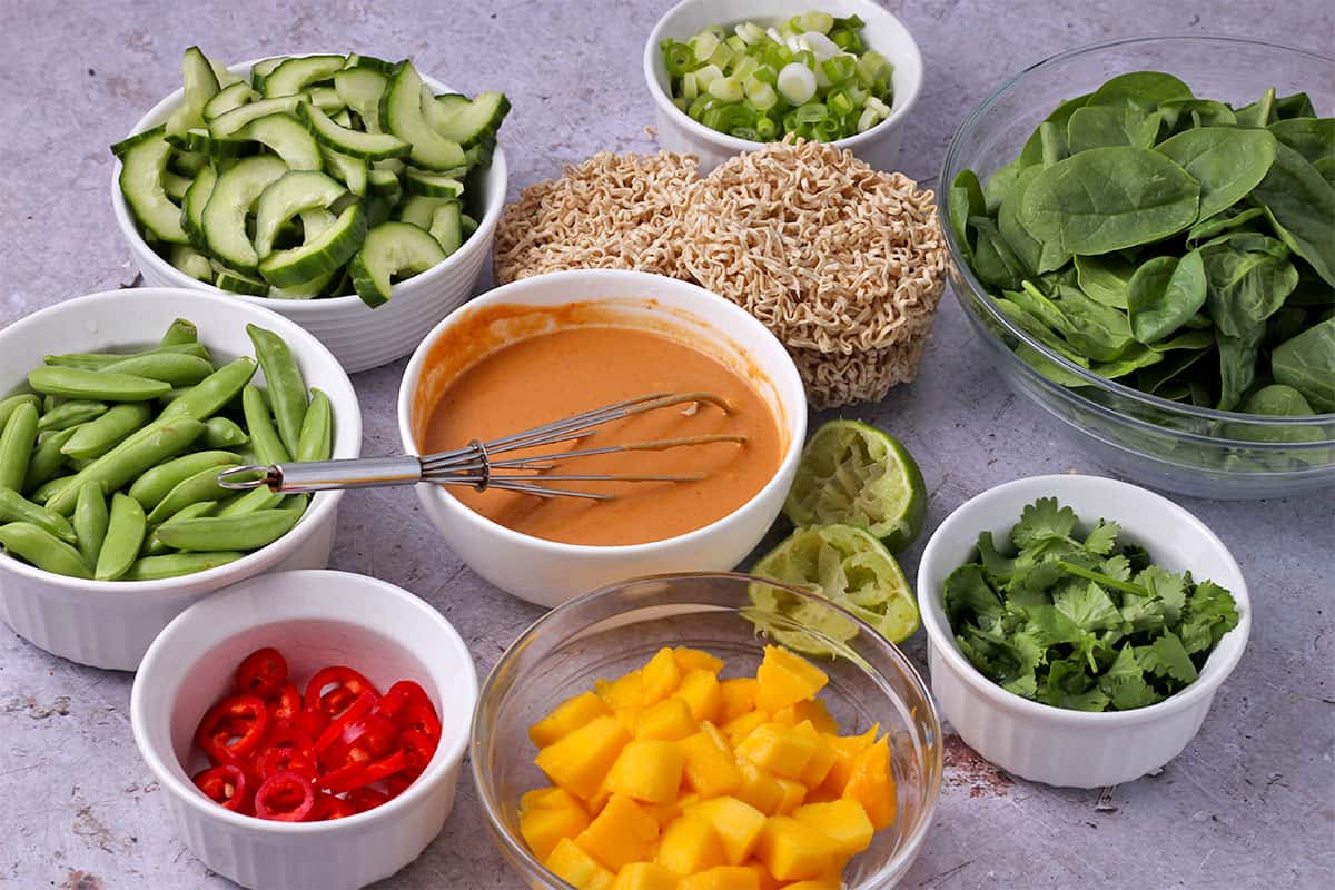The ingredients for peanut sauce noodles and mango salad in small bowls.