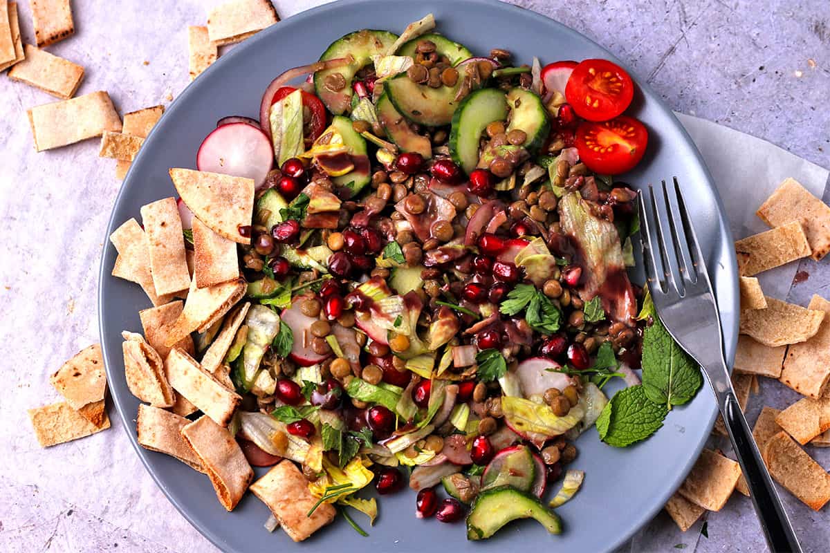 Salad with lentils, vegetables, pita chips, and dressing on a blue plate.