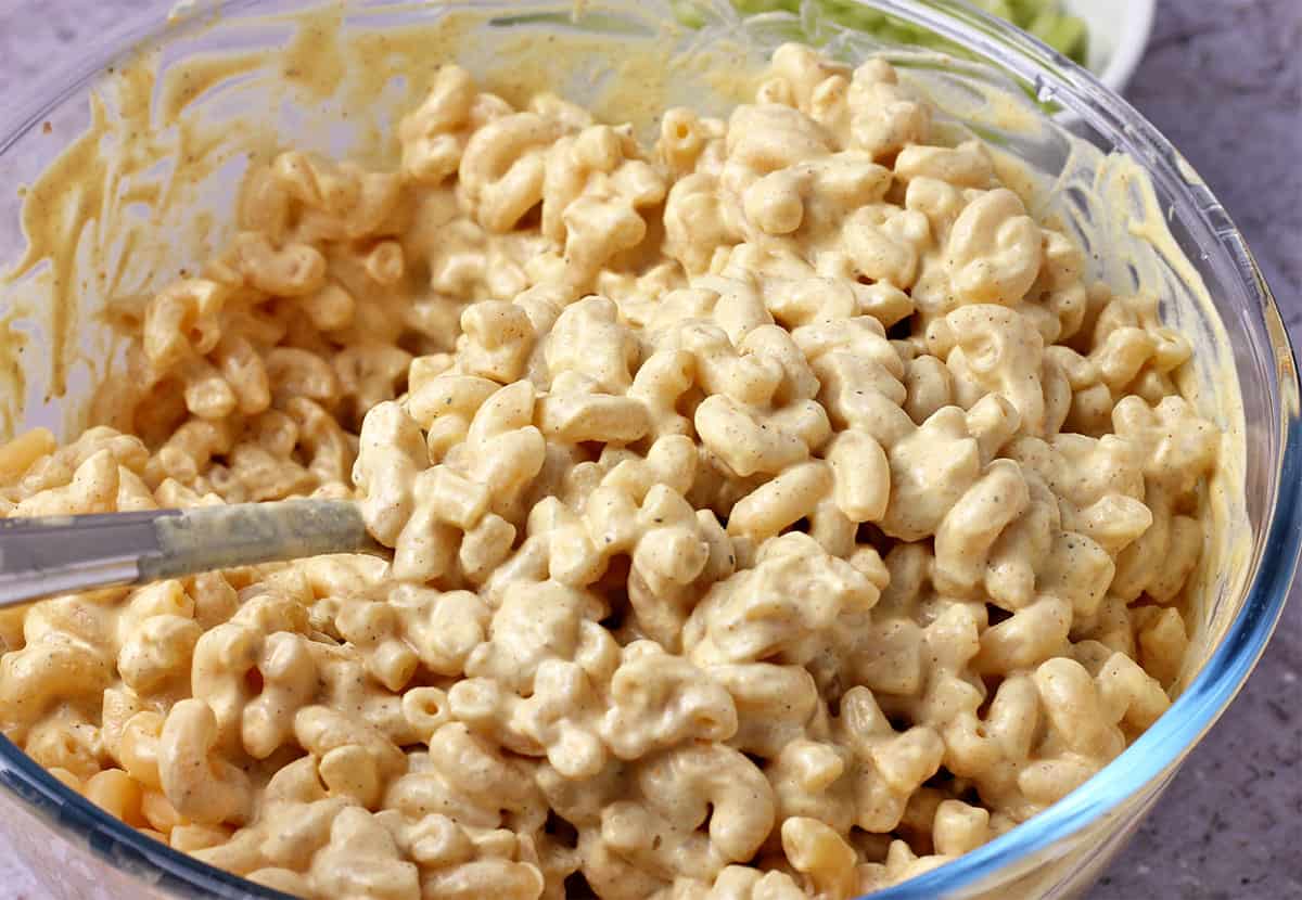Creamy dressing is mixed into a bowl of cooked macaroni.