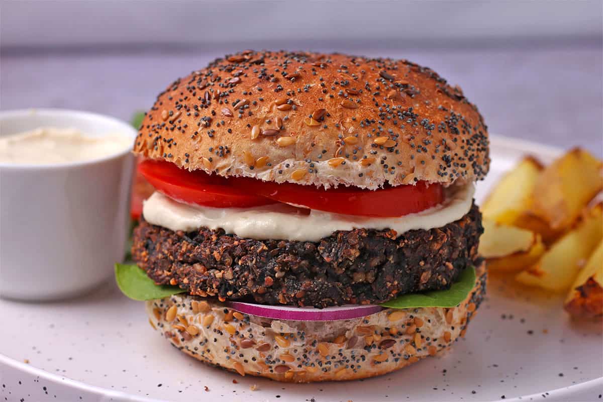 A mushroom burger in a bun with mayo, tomato, lettuce, and red onion.