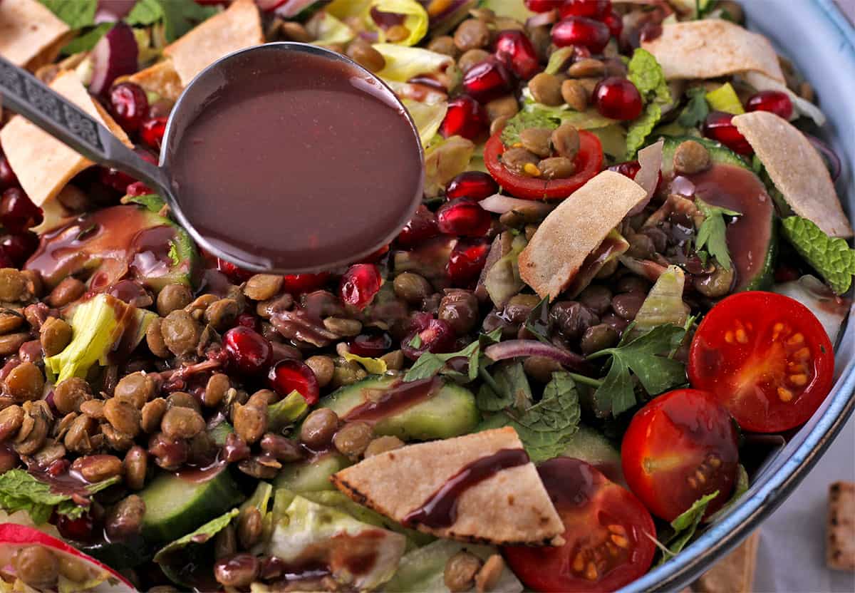 Dressing is added to a salad with lentils, vegetables, and pita chips.