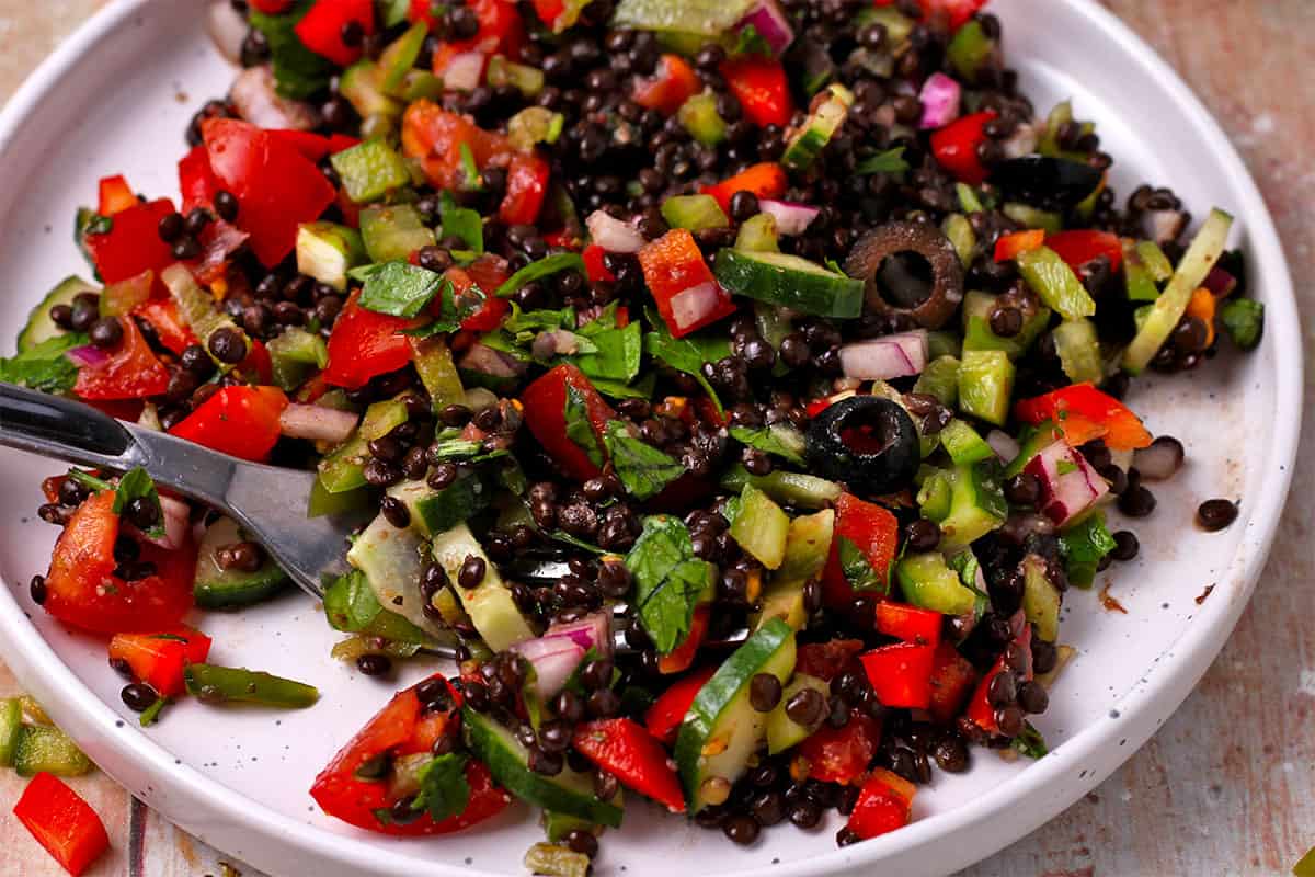 A plate of black lentil Greek salad with a fork.