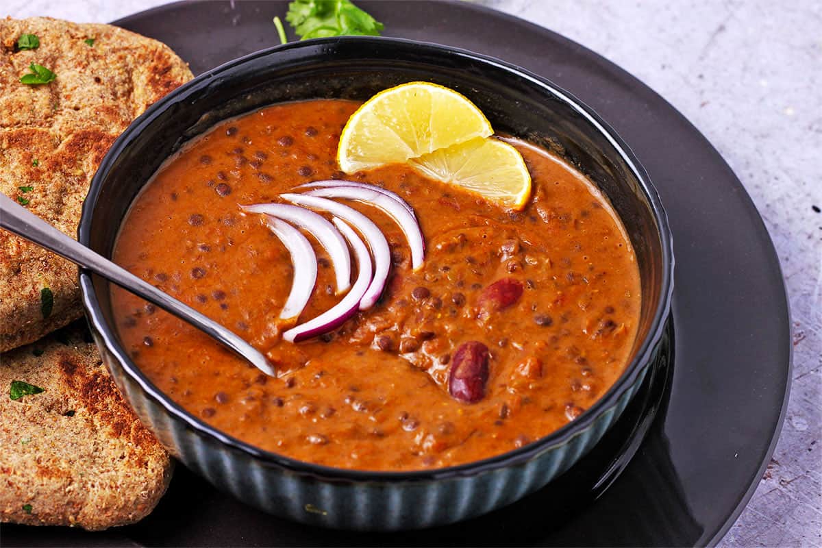 A blue bowl with Instant Pot dal makhani topped with red onions and lemon wedges.