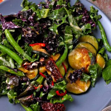 Zucchini and kale salad with green beans, red chili, and sundried tomatoes on a blue plate.