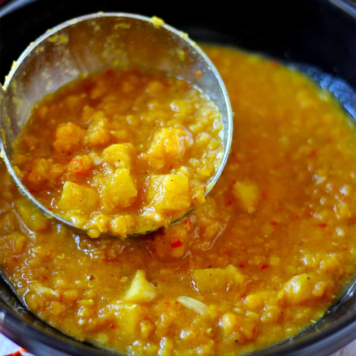 A ladle filled with pineapple and red lentil soup.