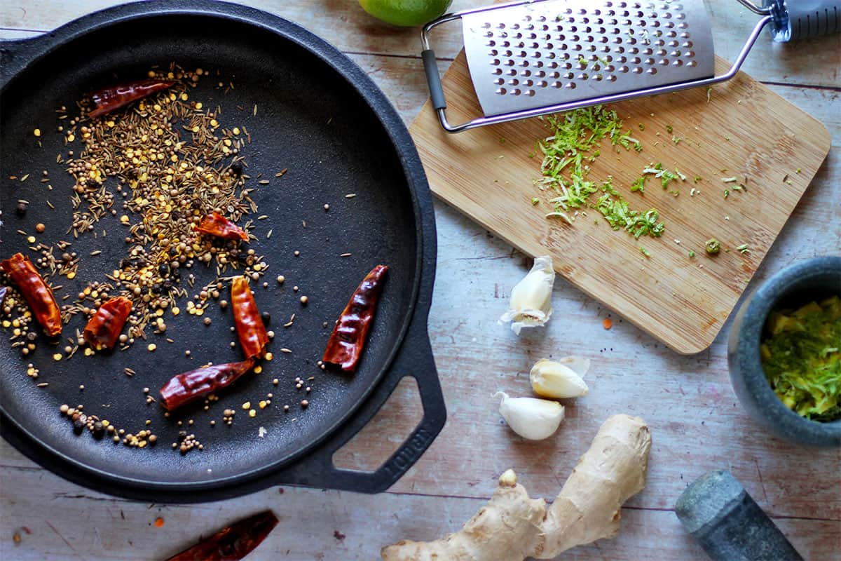Spices in a cast iron skillet with ginger, garlic, and lime zest.