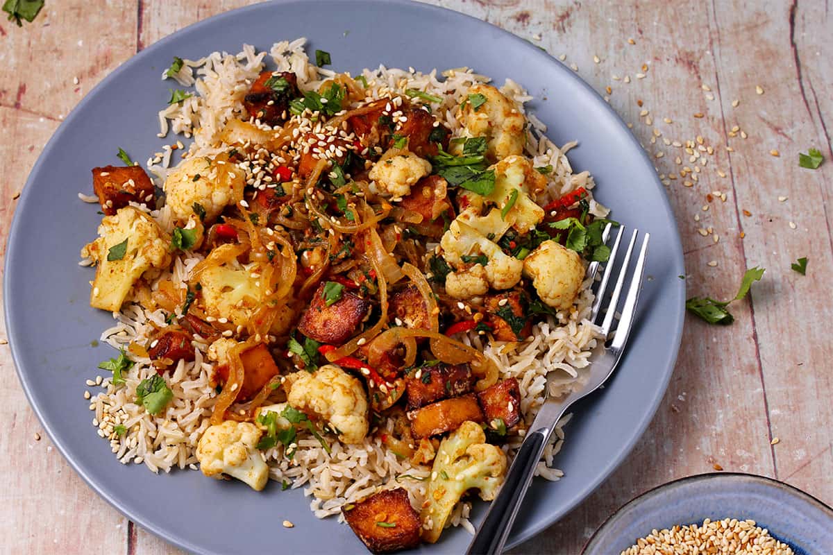 Cauliflower and baked tofu stir fry over rice with coriander and sesame seeds.