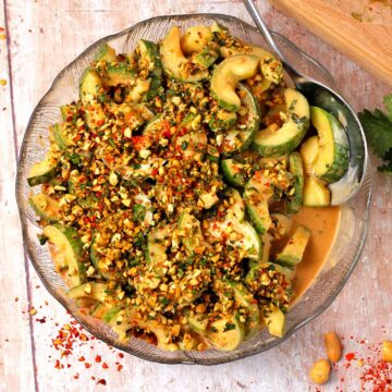 Cucumber salad with peanut dressing topped with chopped cilantro, red chili flakes, and peanuts.