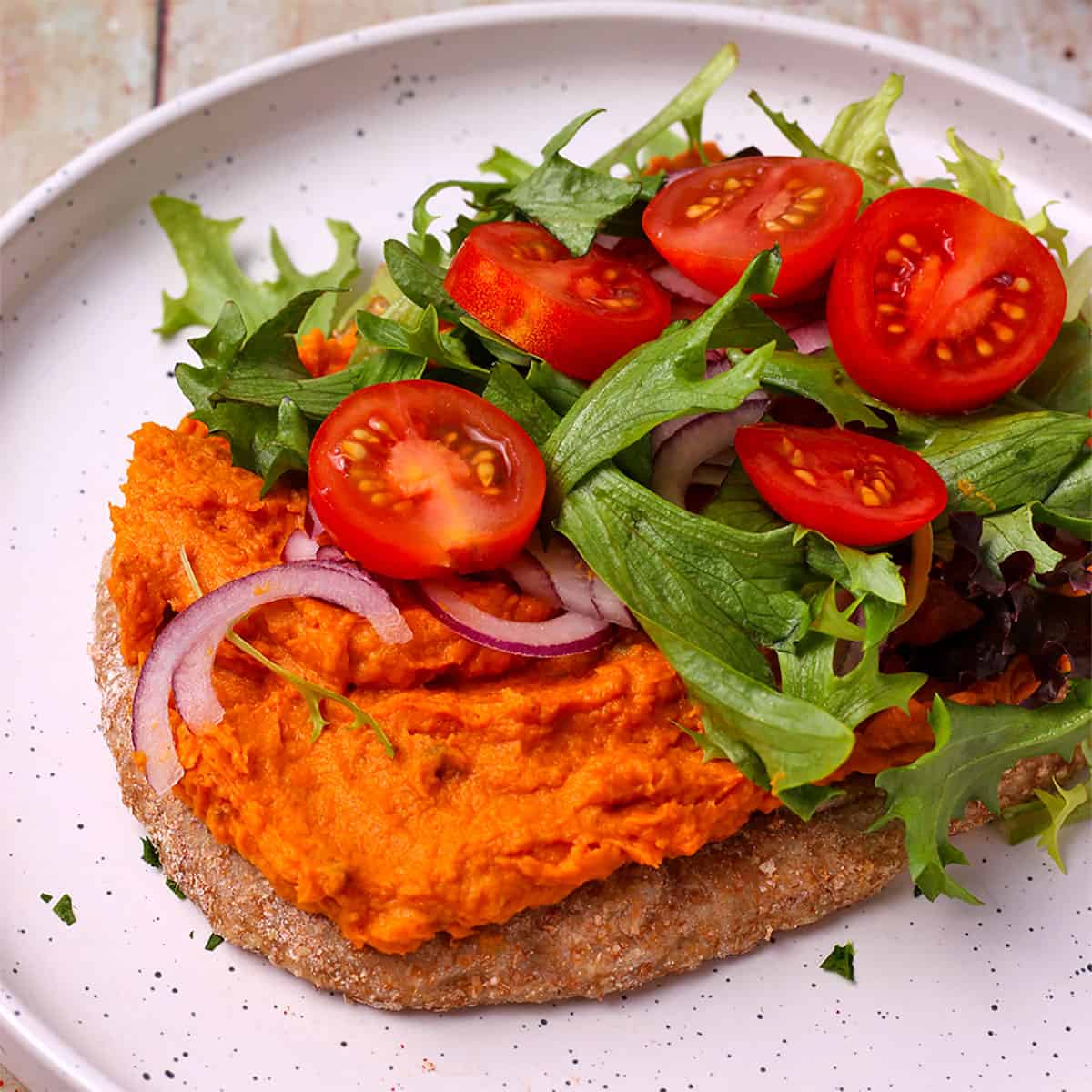 Sweet potato dip is spread on a flatbread with red onions, lettuce, and sliced tomatoes.