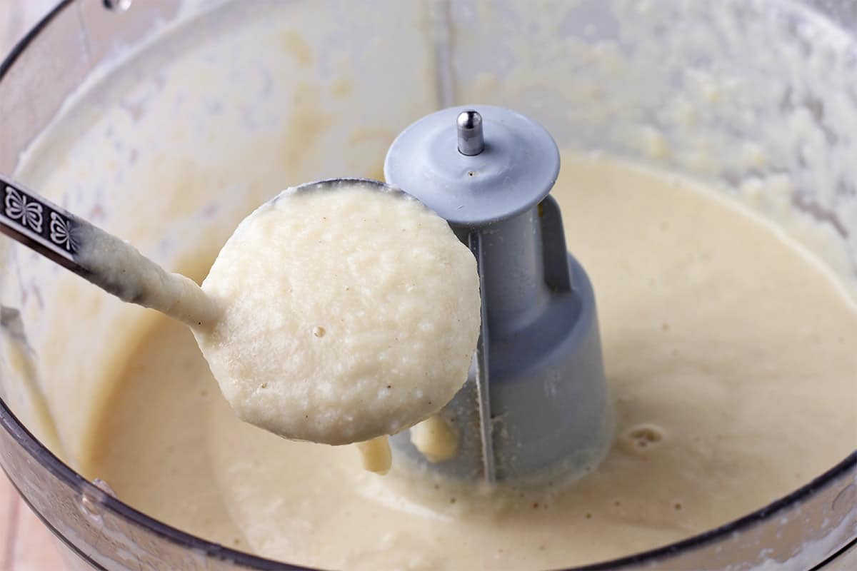 White sauce is blended in a food processor and lifted with a small ladle.